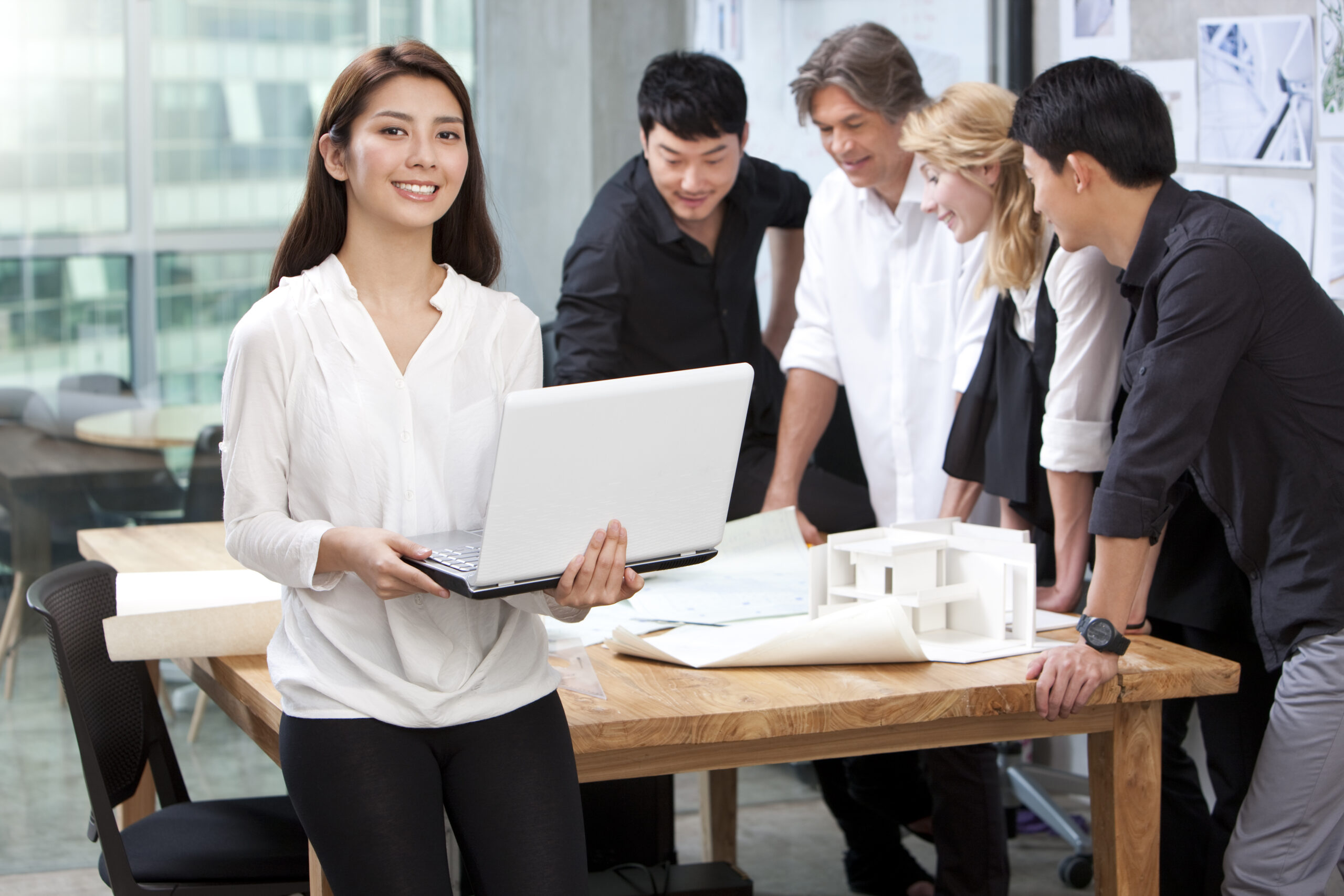 Chinese architect holding laptop in studio with her team in background